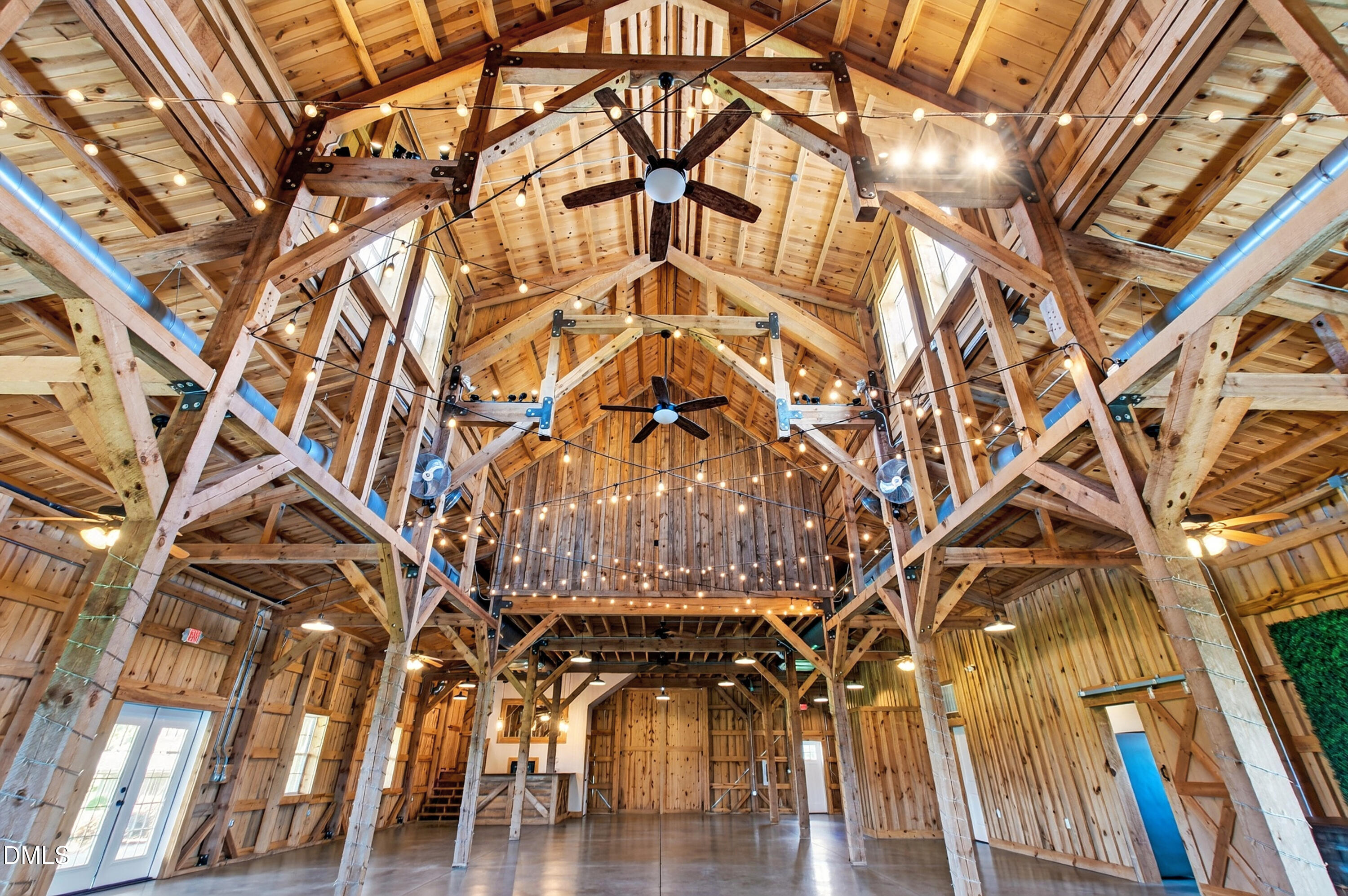 Timber-framed barn interior with a loft, ceiling fans, string lights, and polished concrete floor.