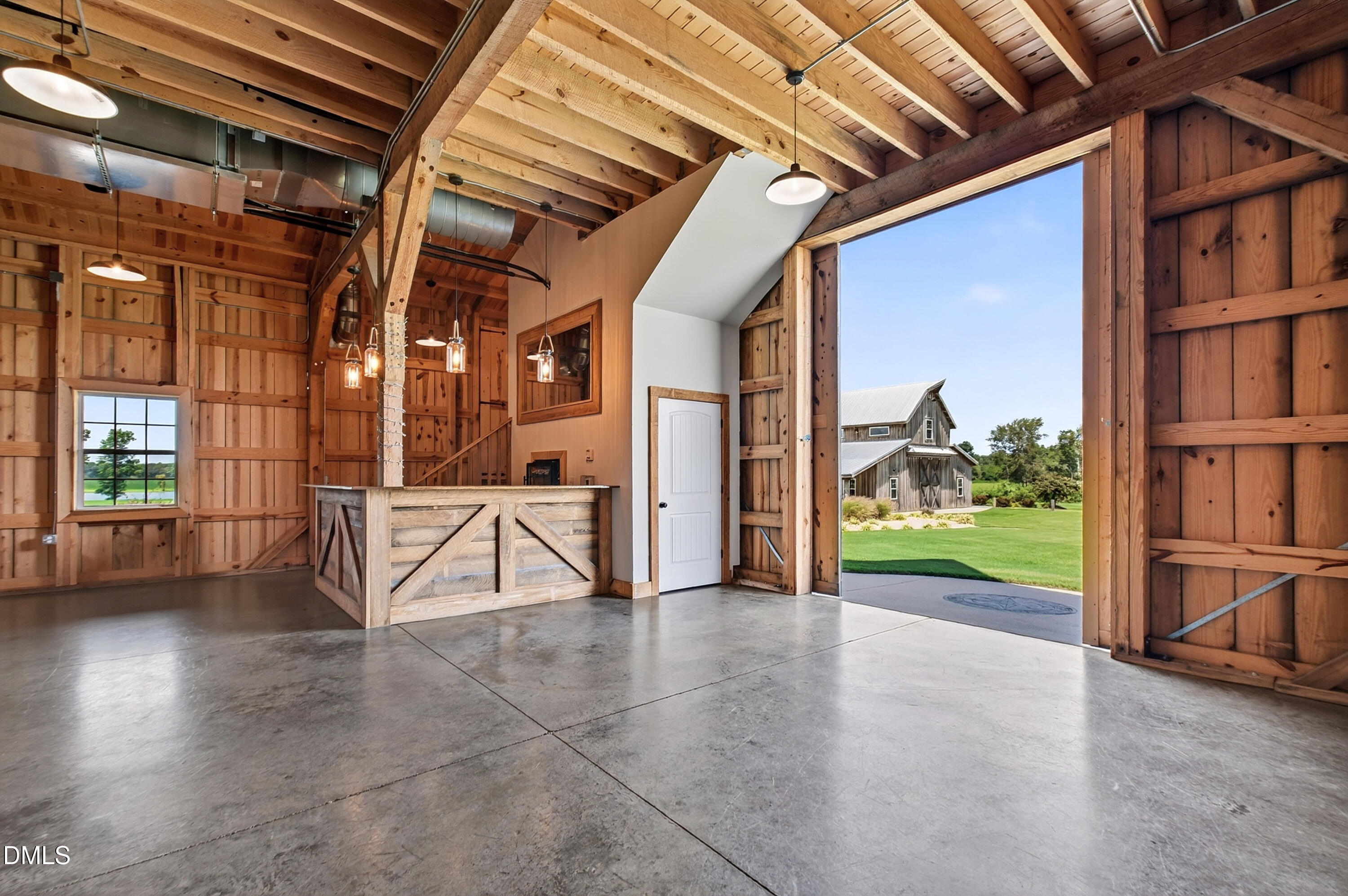 Timber-framed barn interior with a rustic counter and open bay door facing a green lawn.