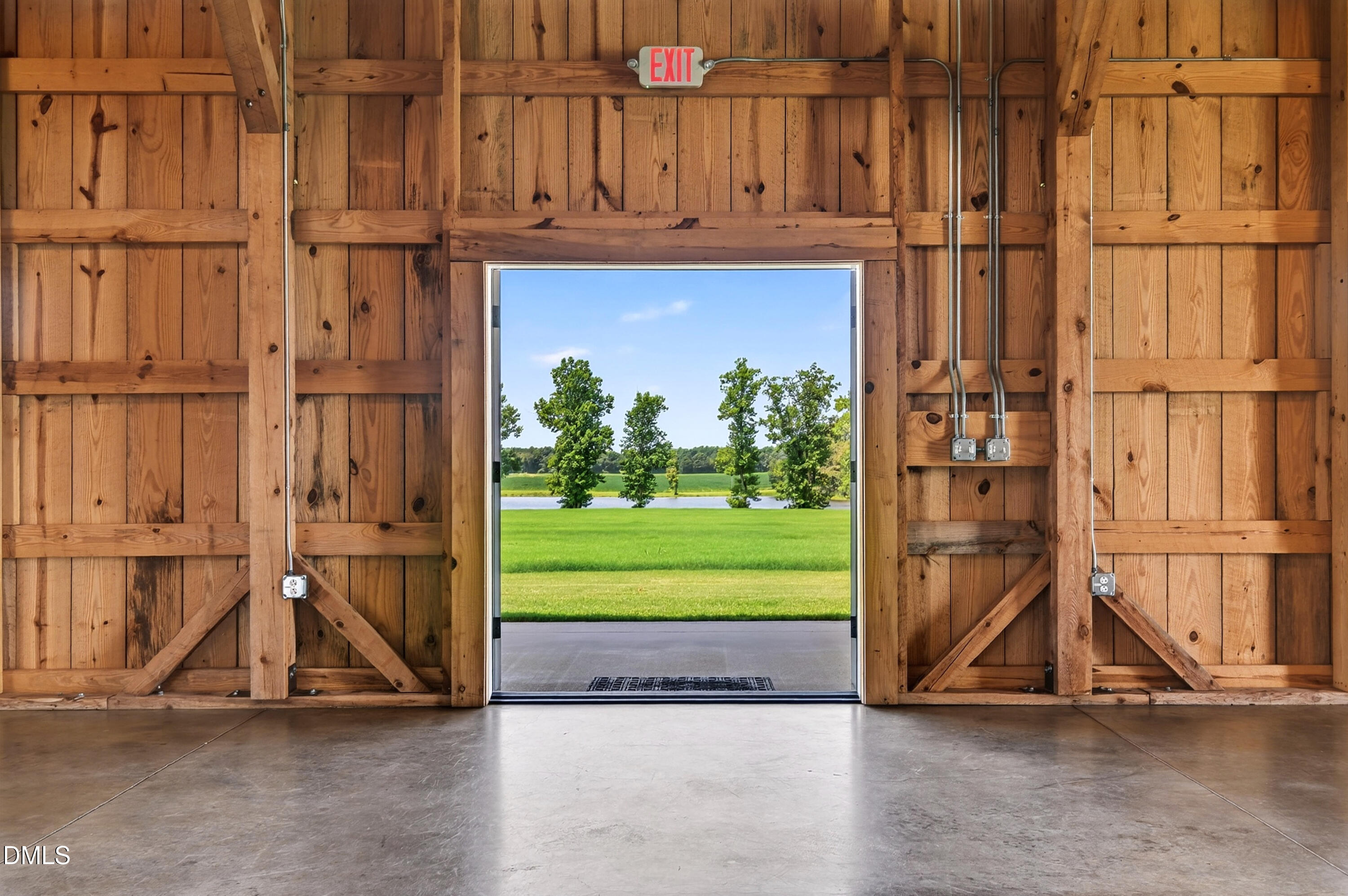Wooden barn interior with an open doorway overlooking a green lawn, trees, and pond.