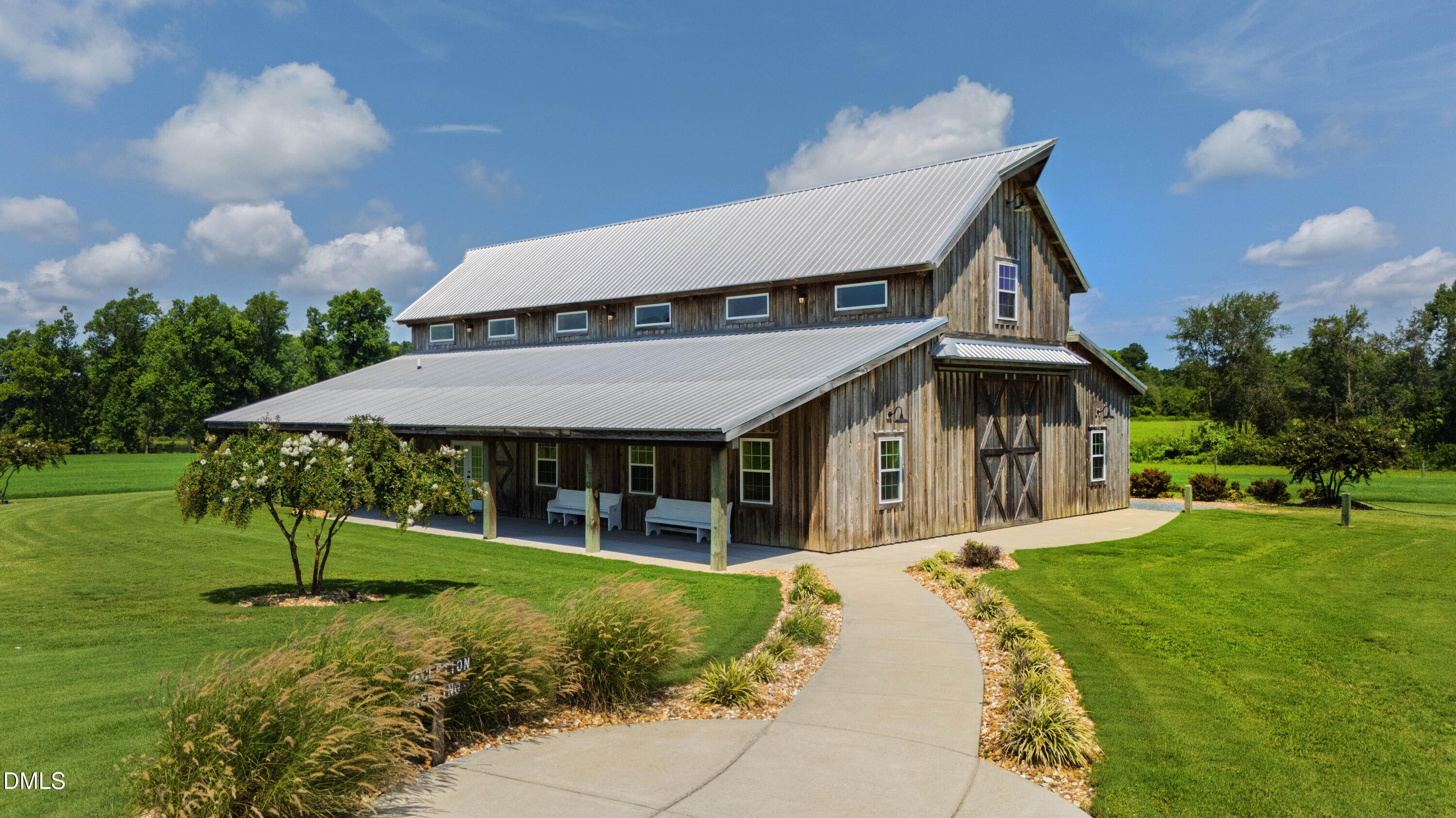 Weathered-wood barn-style building with a metal roof, covered porch, and curved walkway across a green lawn.