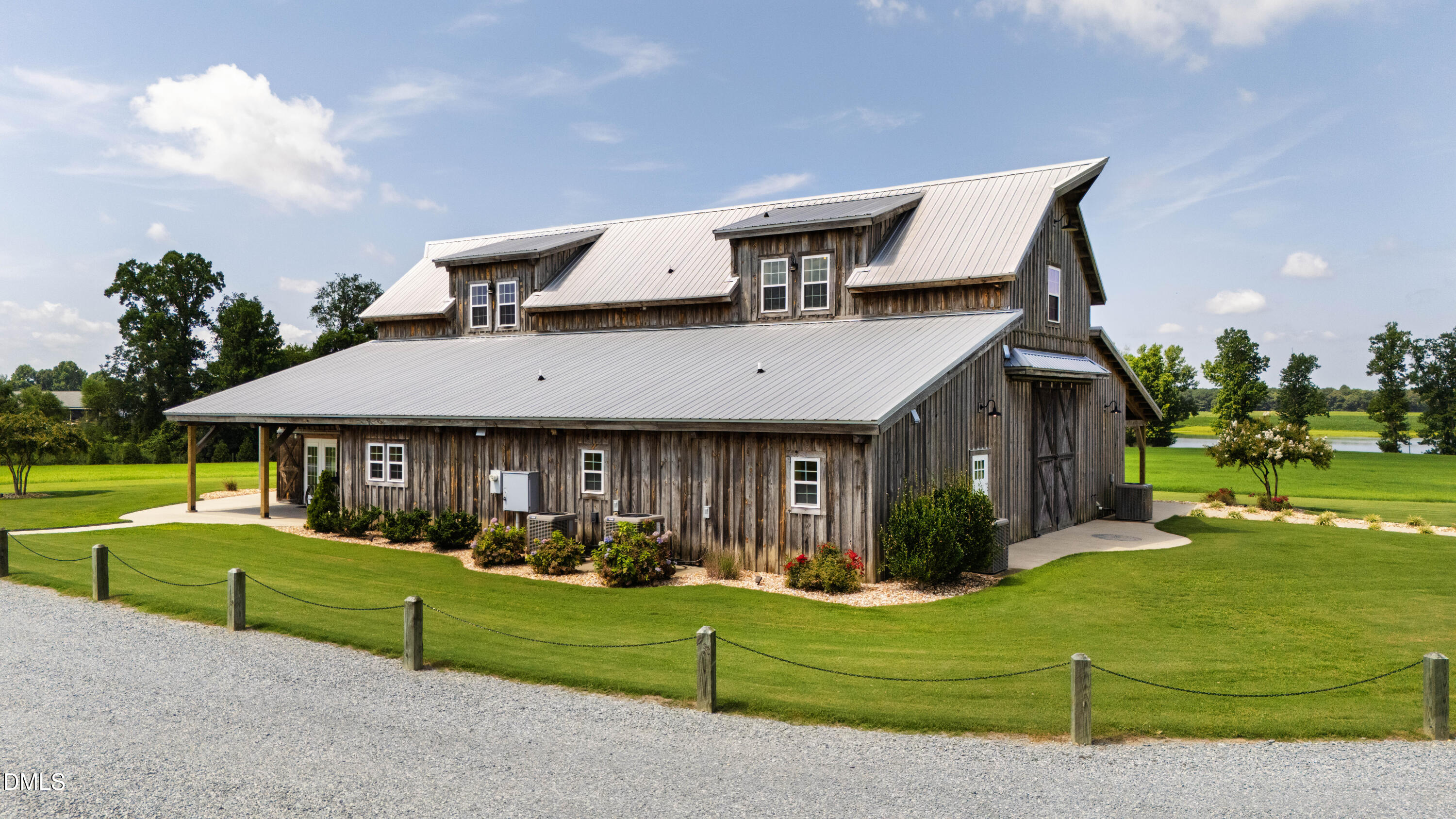 Rustic wooden barn-style property with a light metal roof beside a manicured lawn and pond.