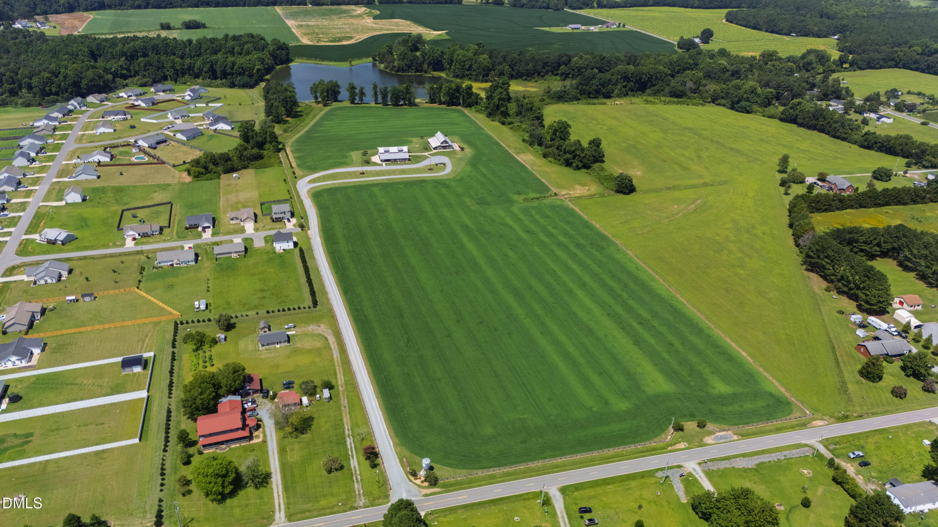 Aerial view of a large green field beside a road, with homes and a pond.