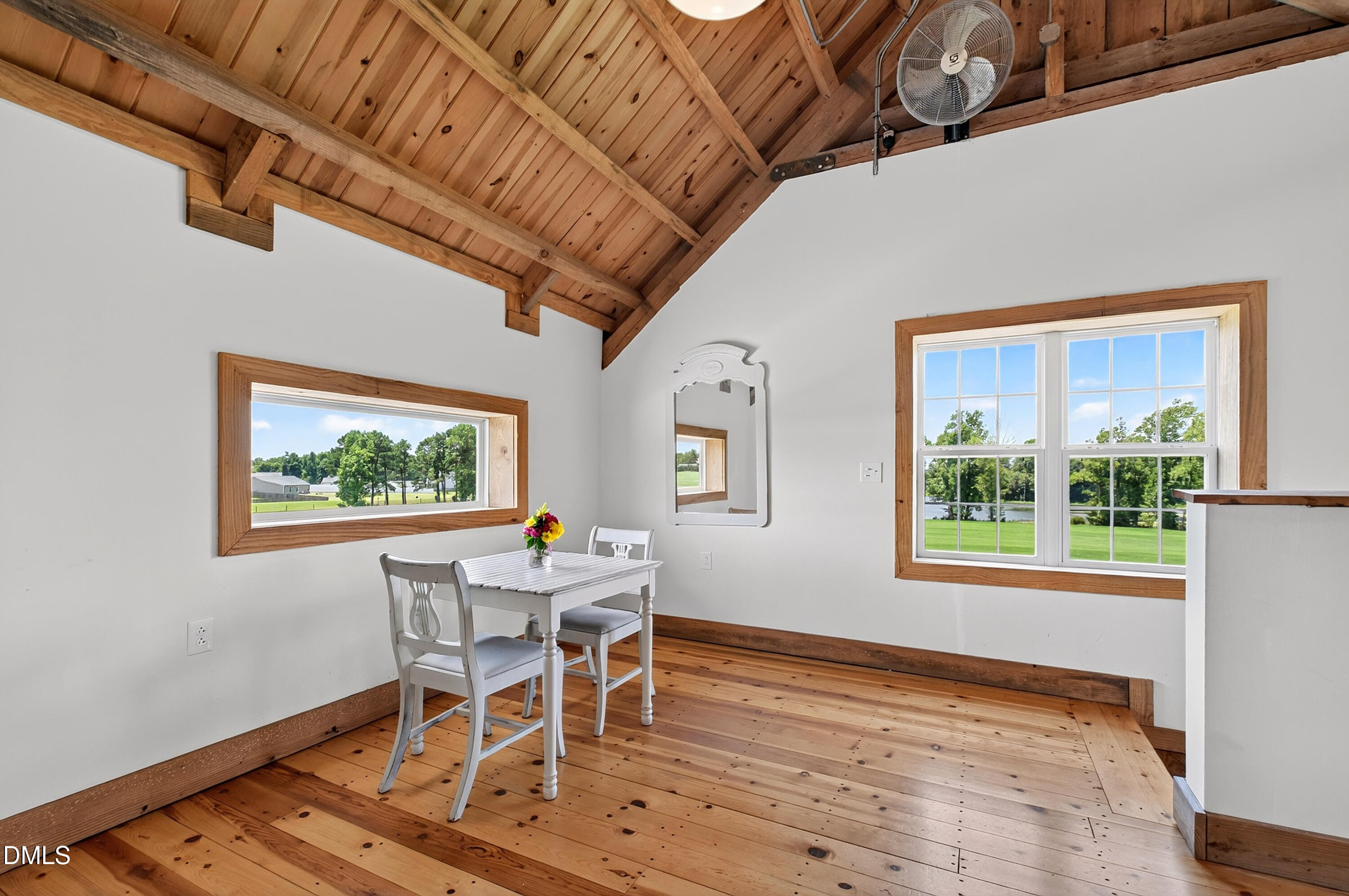 Dining nook with exposed wood ceiling, pine floors, and windows overlooking a lawn and pond.