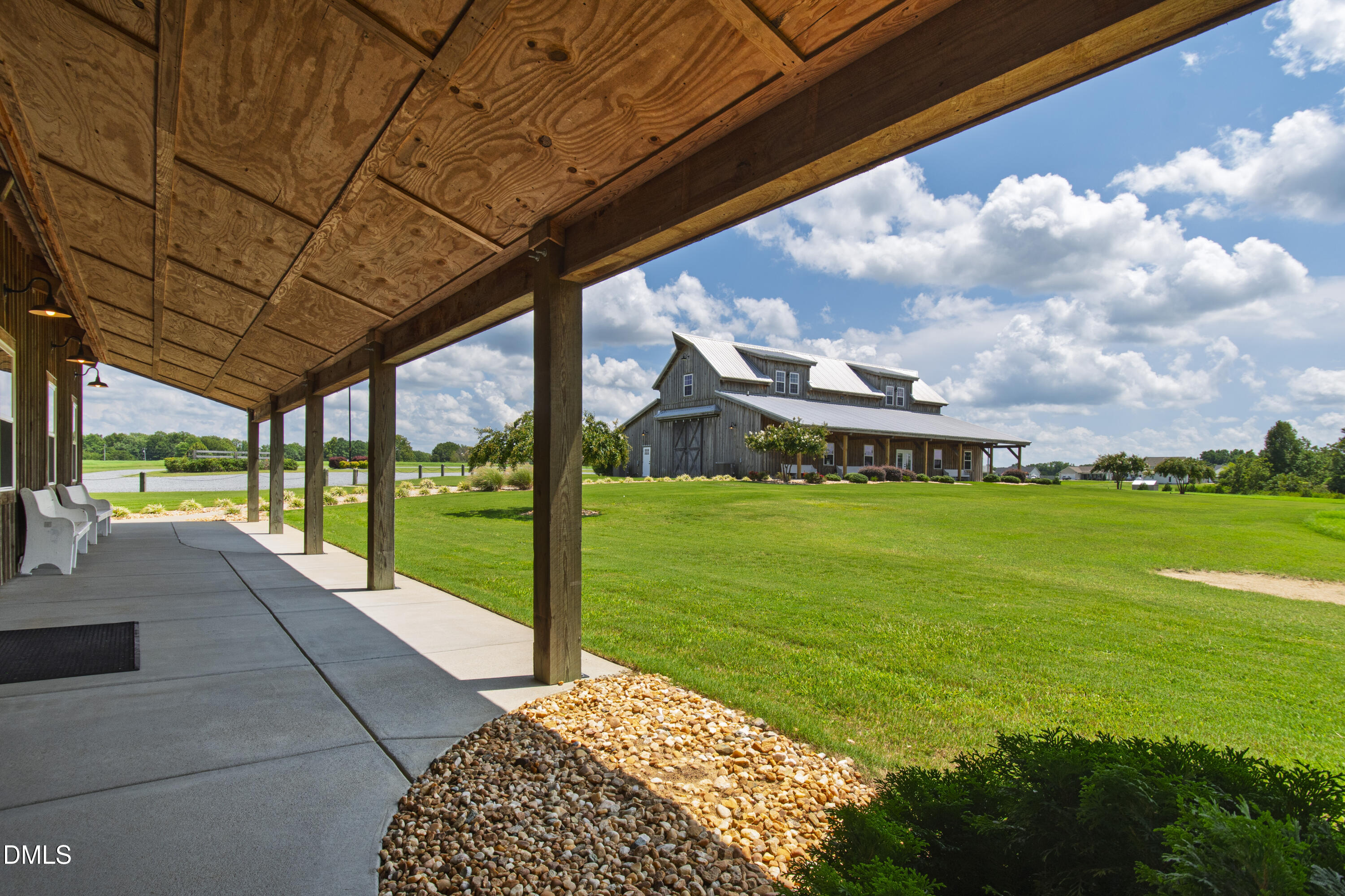 Barn-style home beyond a covered porch, with a broad green lawn and landscaped grounds.