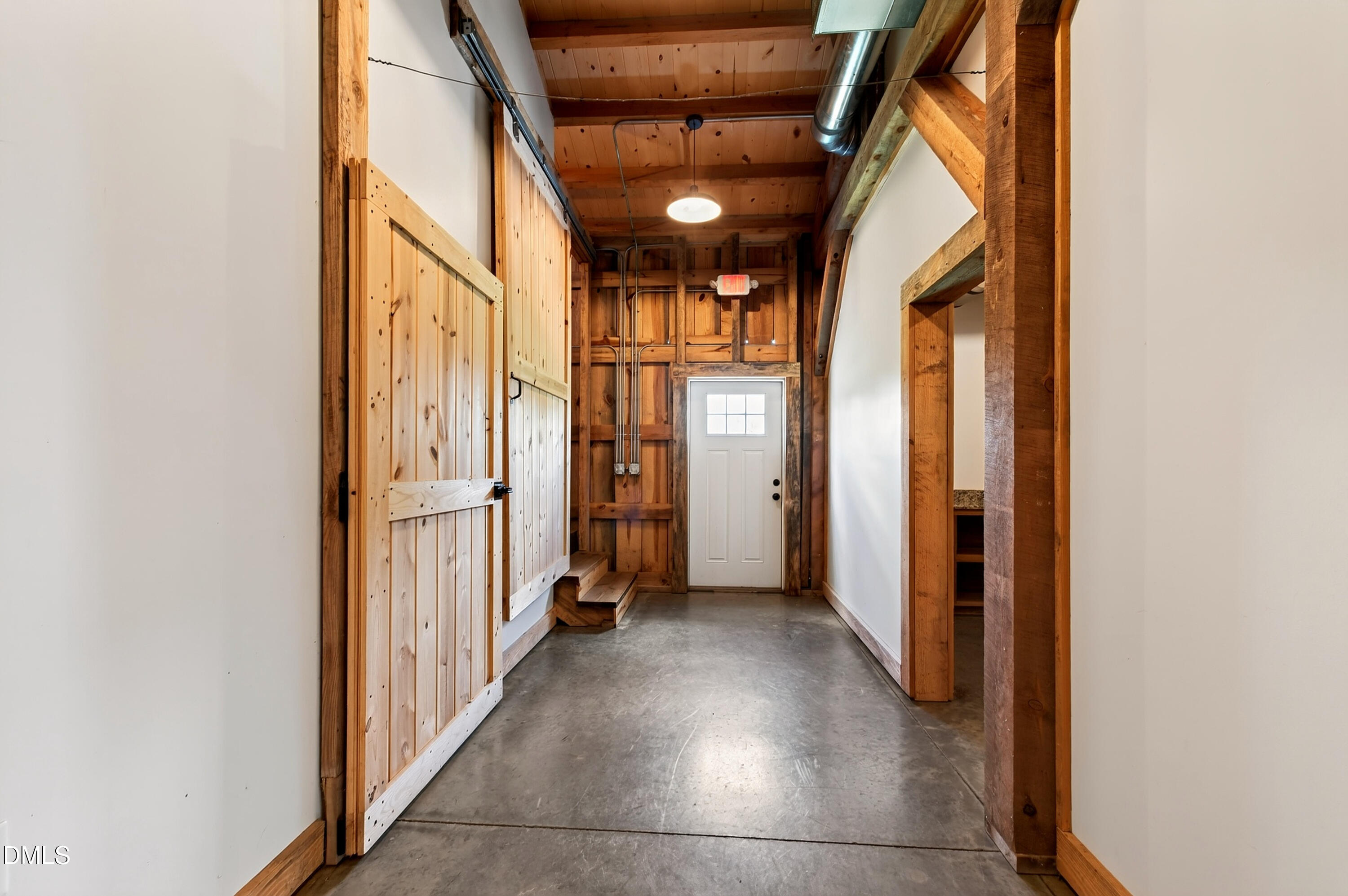 Hallway with concrete flooring, exposed timber framing, sliding barn doors, and a white door at the far end.