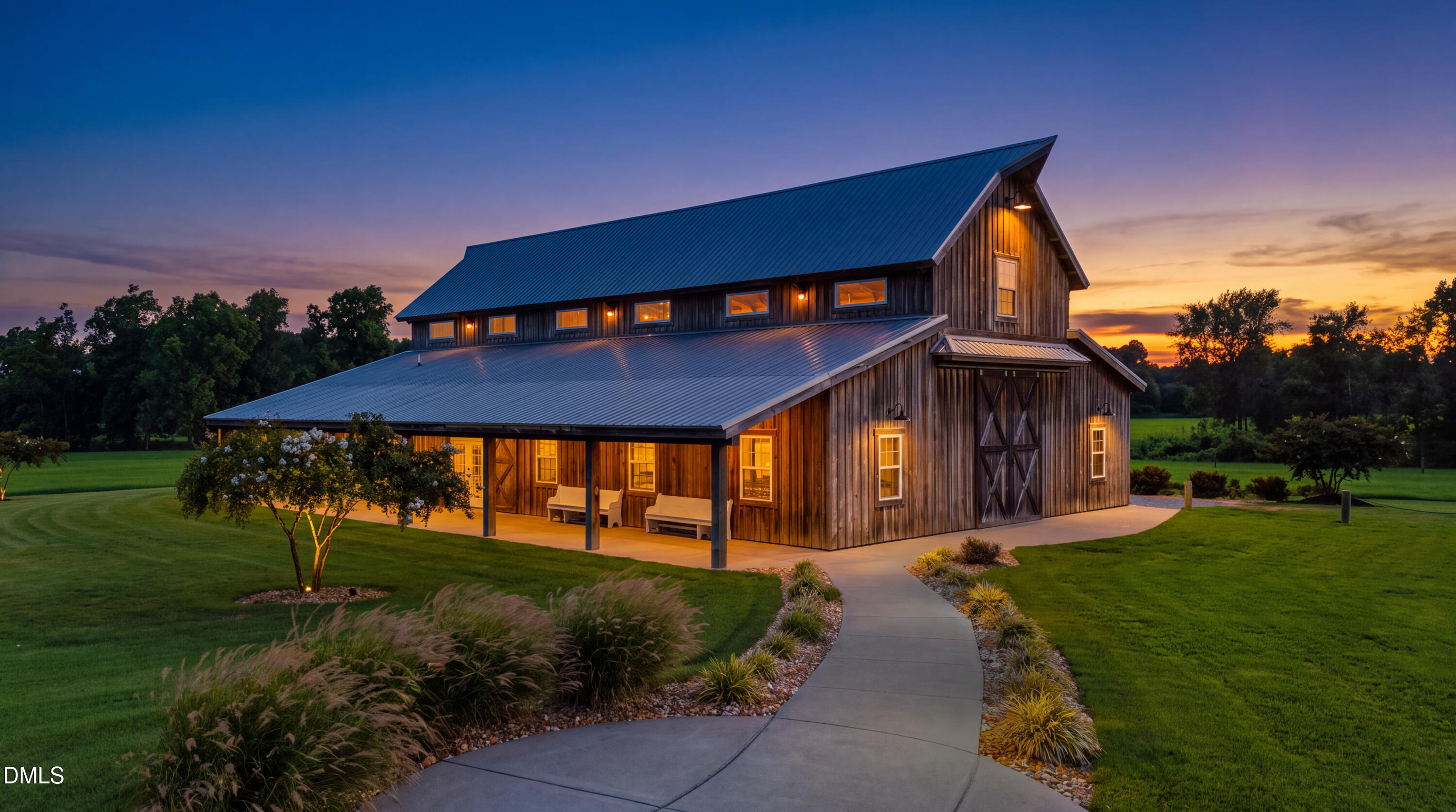 Barn-style home with weathered wood siding and a blue metal roof, warmly lit at dusk.
