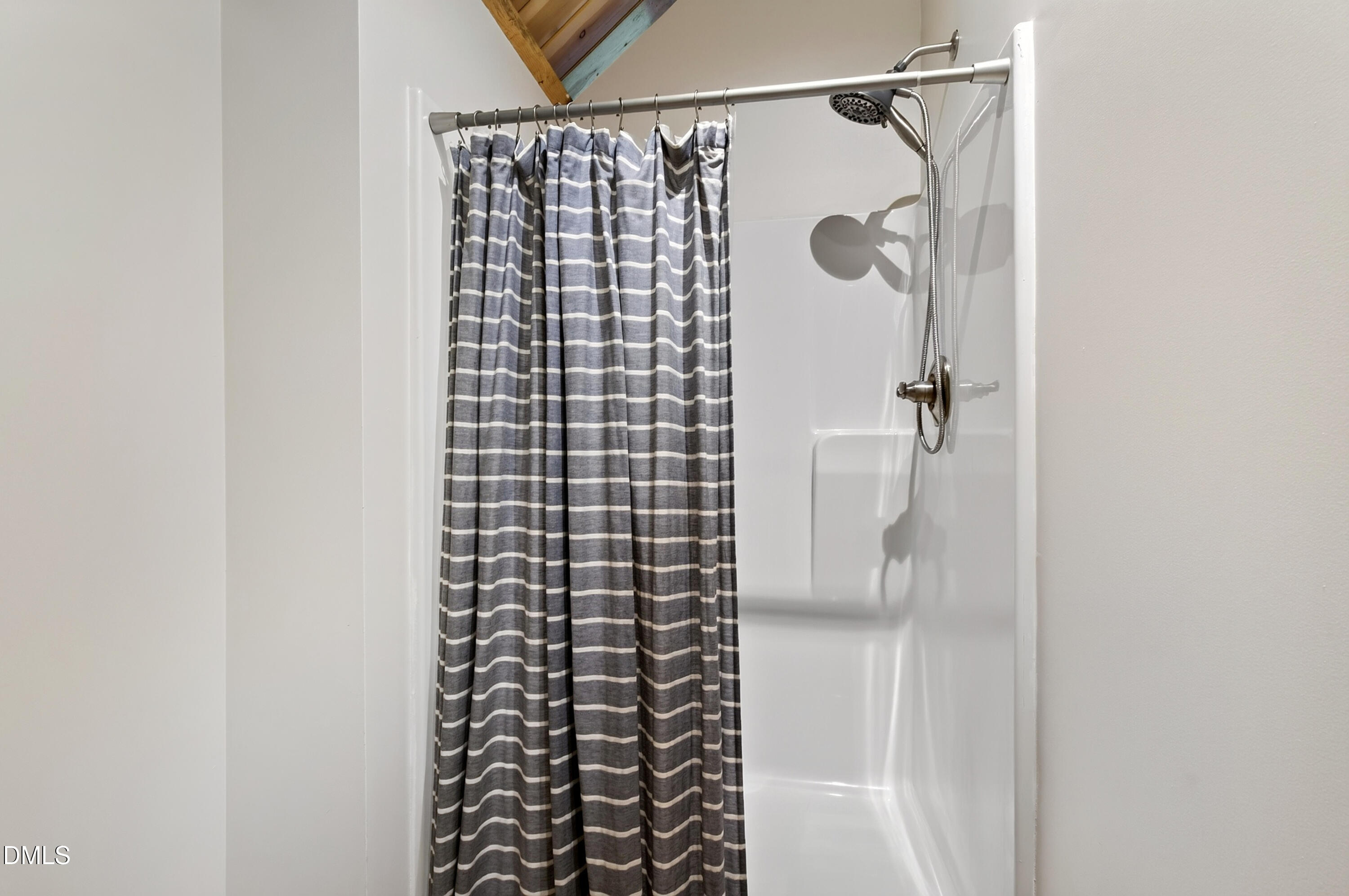 Shower stall with a gray-and-white striped curtain, chrome fixtures, and exposed wood ceiling boards.