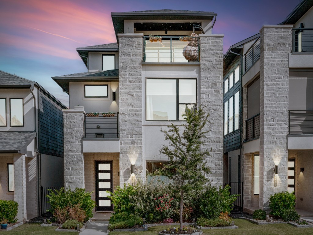 Modern stone-front home with balconies and landscaped yard at dusk