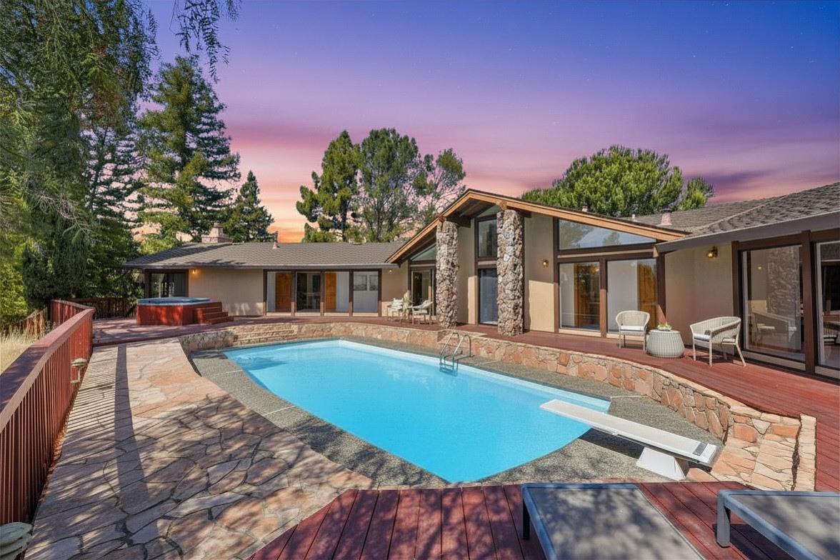 Single-story home with a swimming pool, stone patio walls, and redwood deck at dusk.