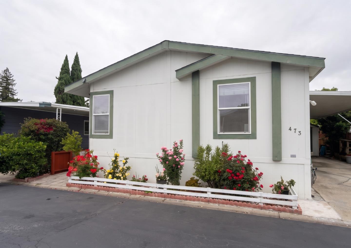 White home with sage-green trim, flowering front garden, and the number 473 beside the entrance.