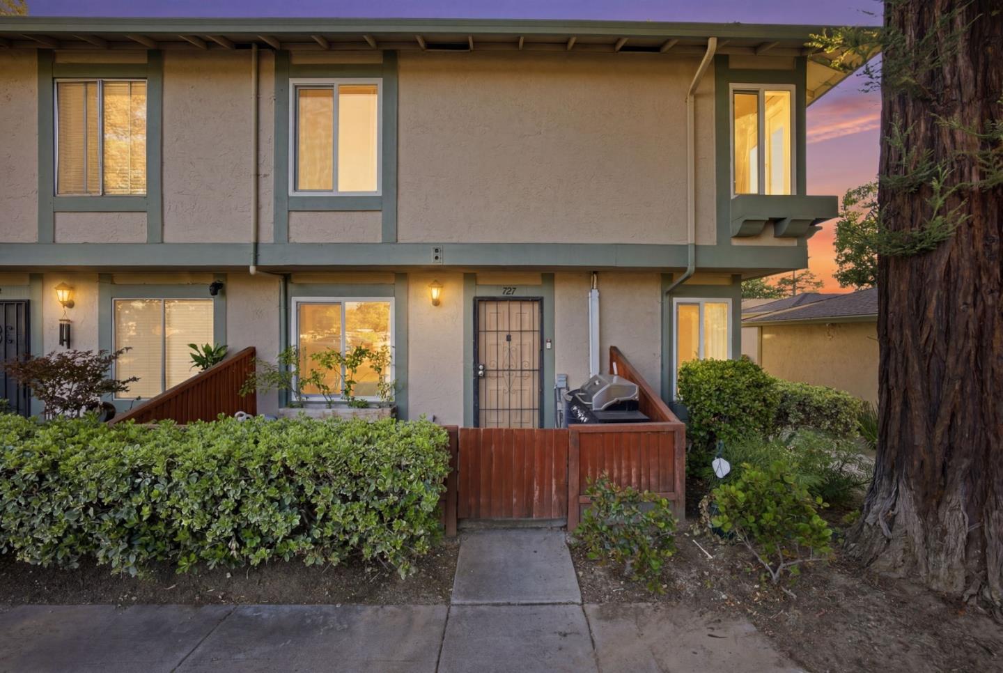 Two-story townhouse with a wooden entry gate and shrubs at dusk.