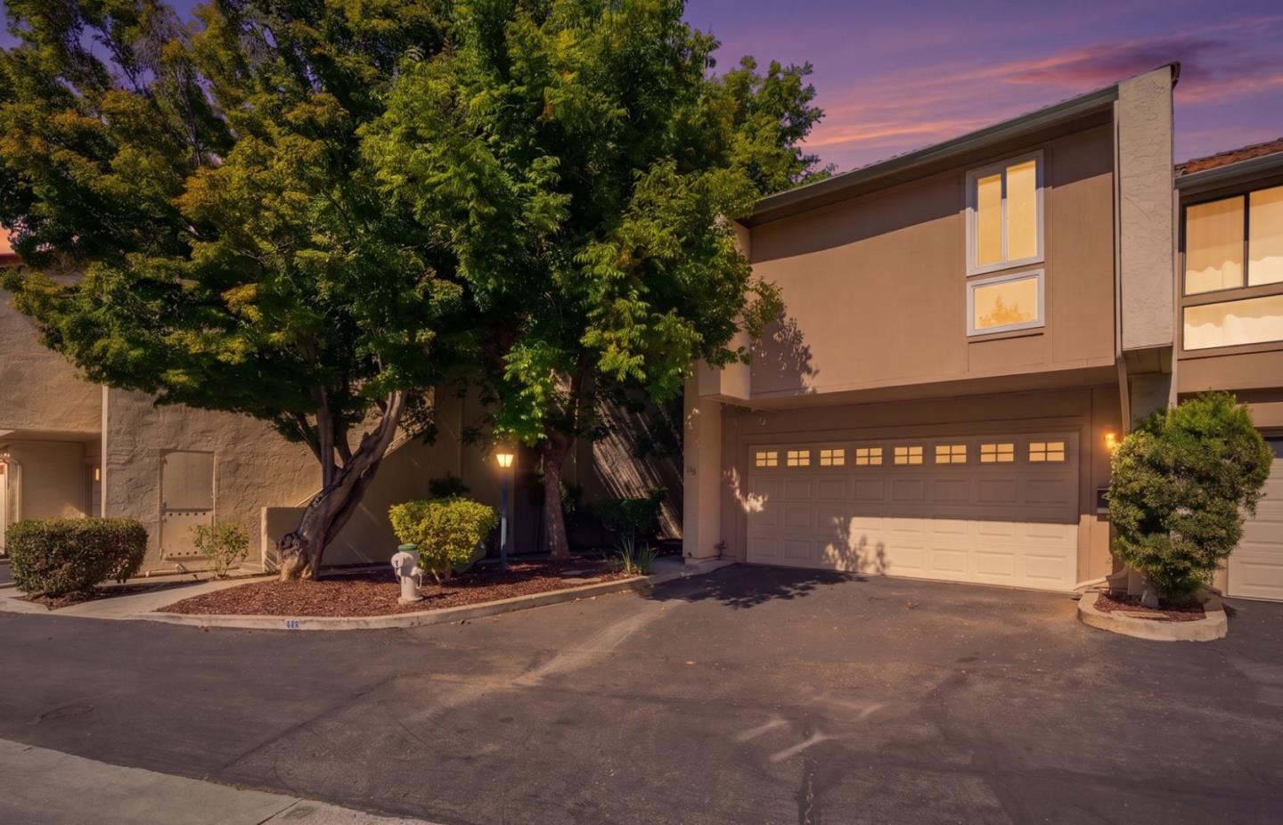 Two-story townhouse with a wide garage and mature trees under a purple dusk sky.