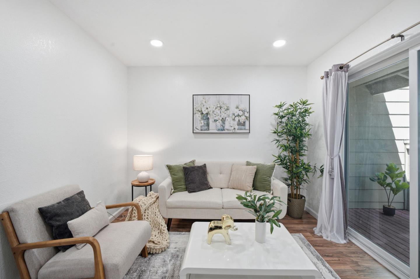 Staged living room with a cream sofa, leafy plants, and sliding glass doors to a deck.