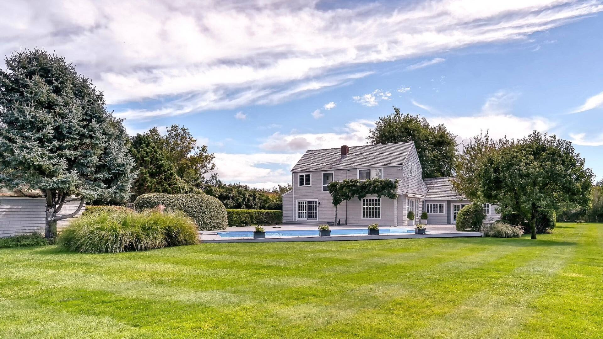 Gray-shingled two-story house with a swimming pool, landscaped grounds, and broad lawn.