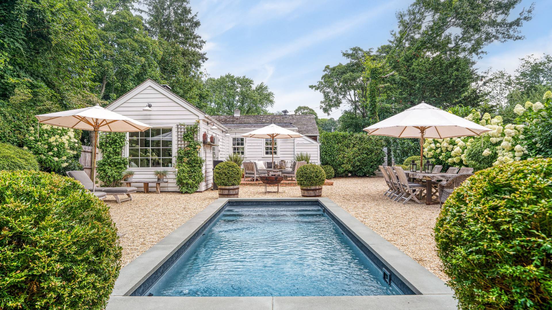 Backyard pool beside a white house, with gravel patio, outdoor dining, and flowering hydrangeas.