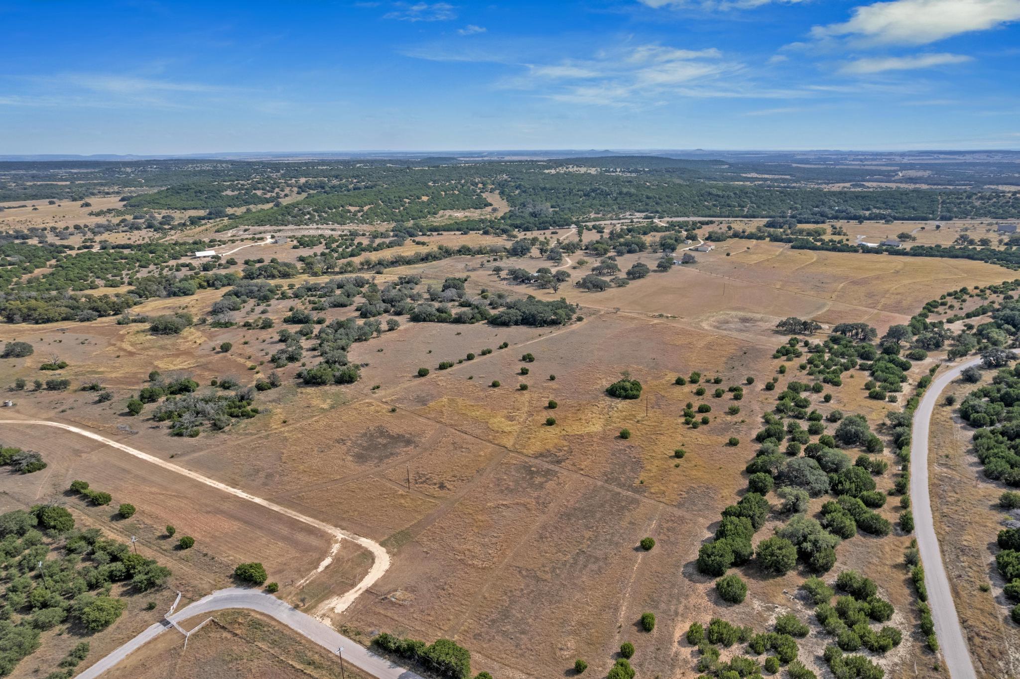 Aerial view of dry rural acreage with scattered trees, open fields, and roads.
