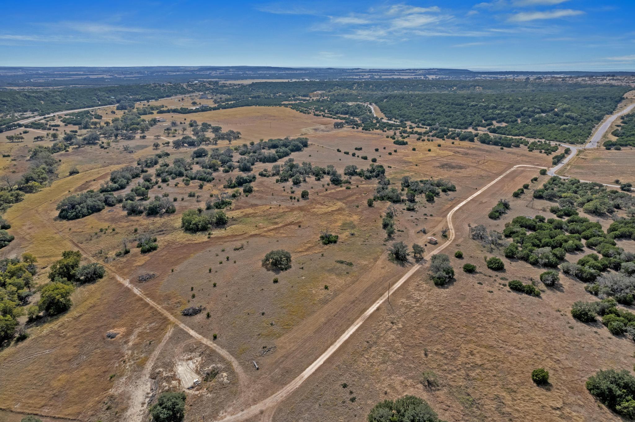 Aerial view of dry pastureland with scattered trees and winding dirt access roads.