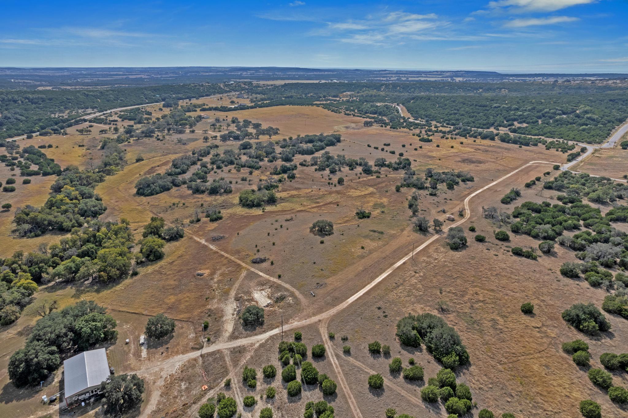 Aerial view of dry rural acreage with scattered trees, dirt tracks, and a small building.
