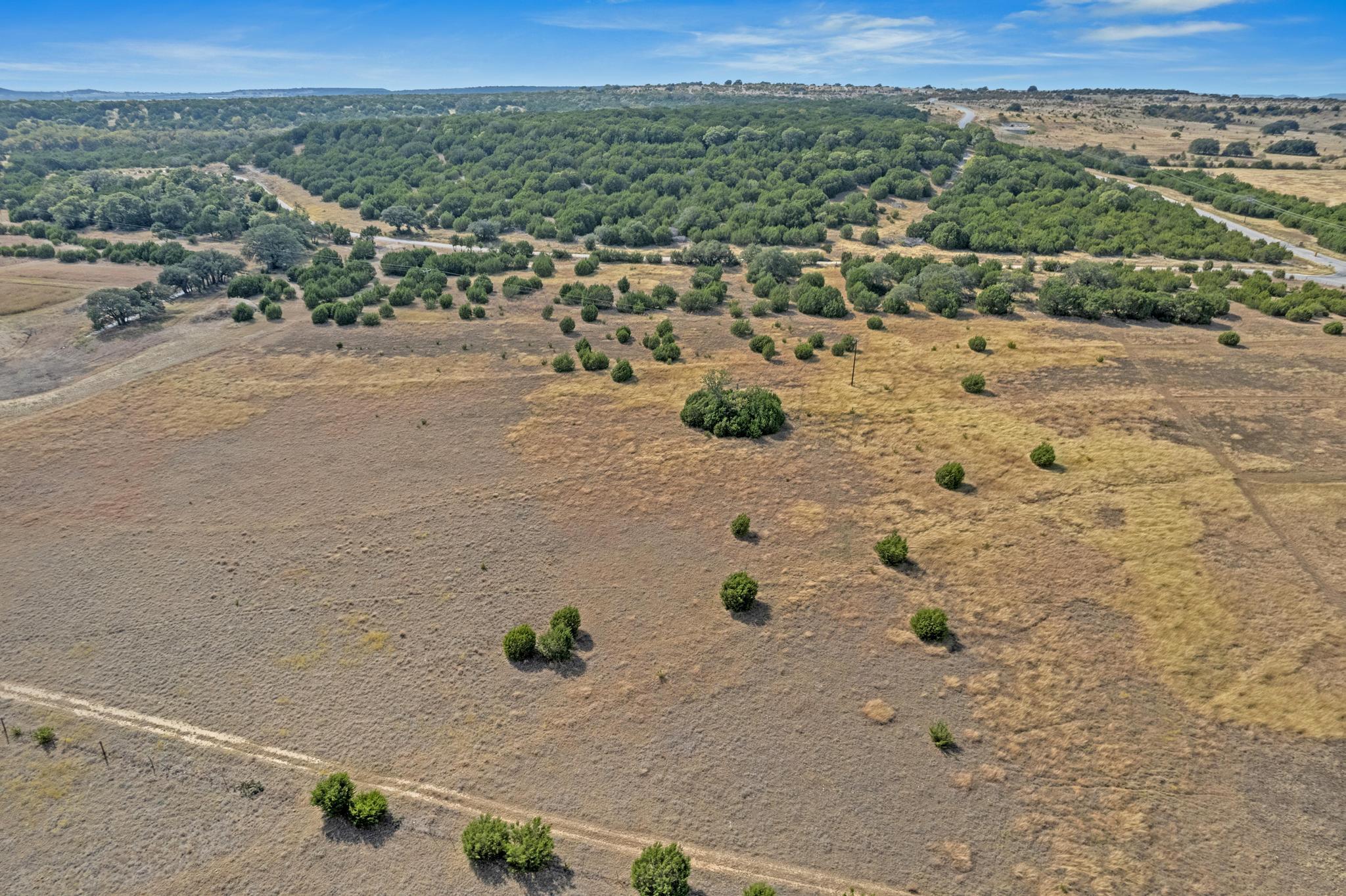 Aerial view of dry rural land with scattered shrubs, tree cover, and dirt tracks.
