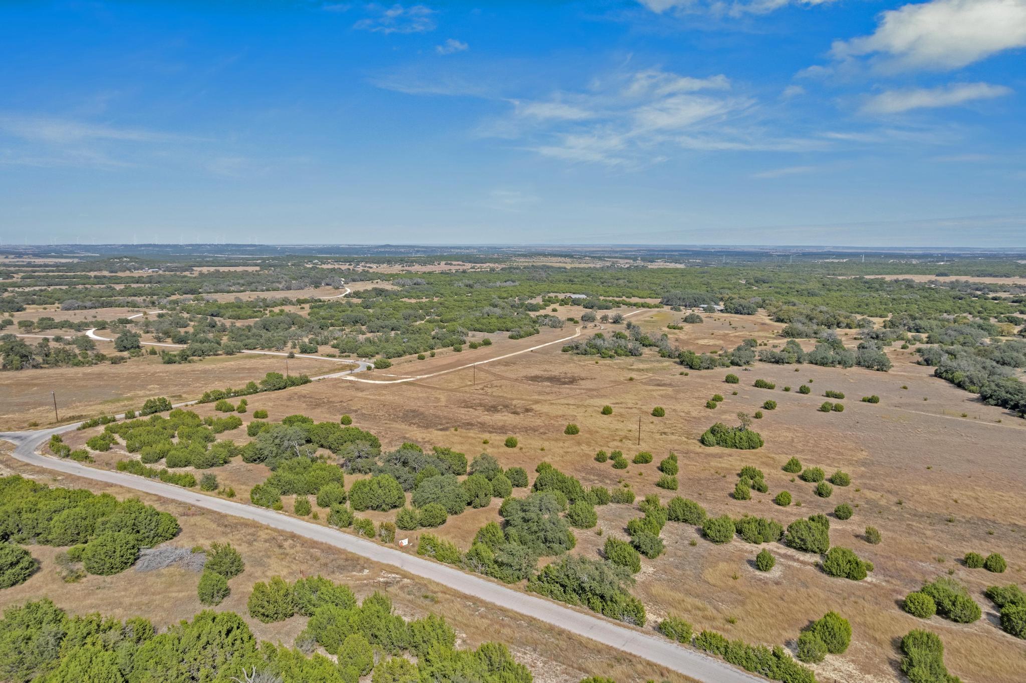Aerial view of open rural land with scattered shrubs and winding roads.