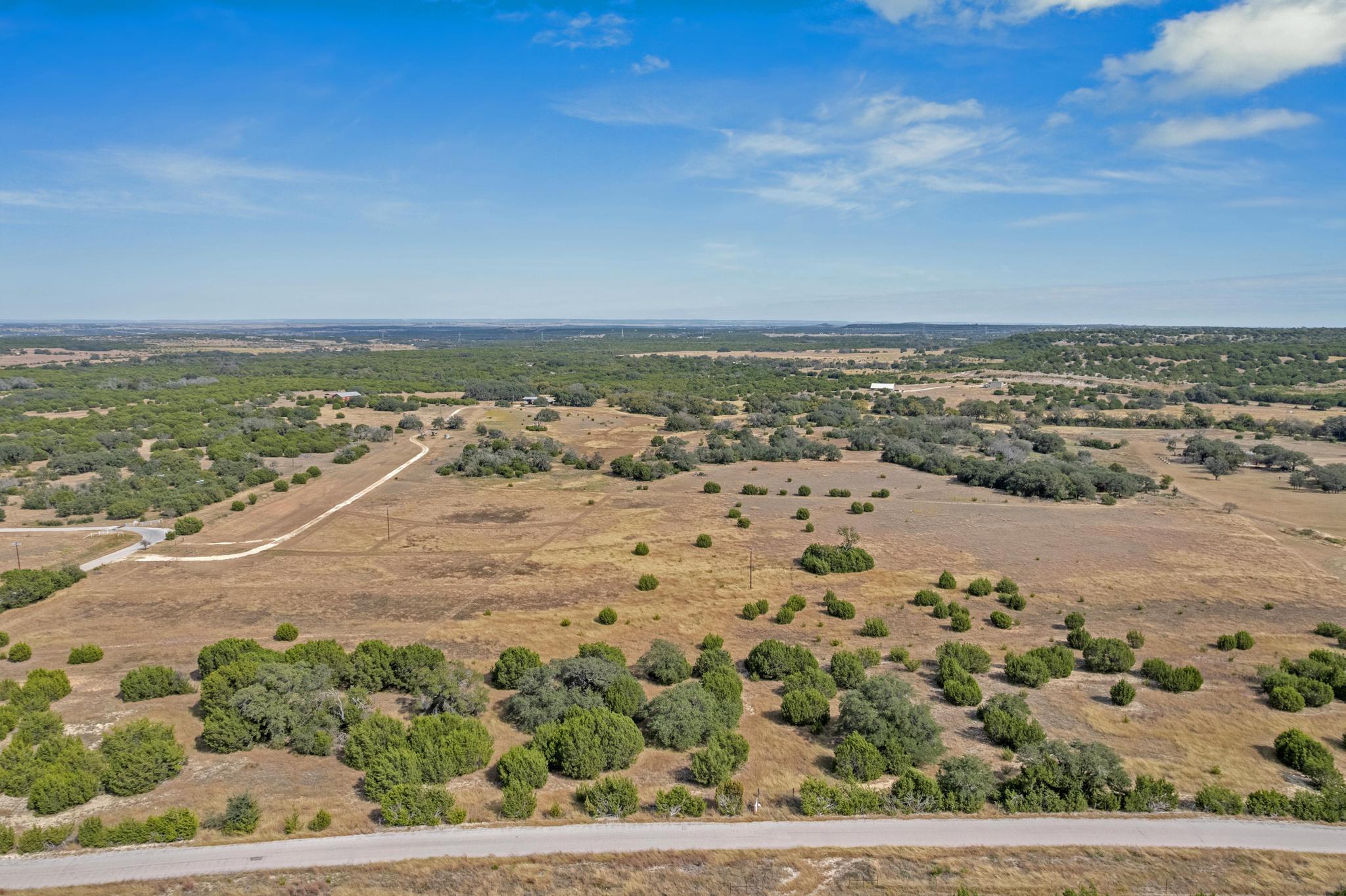 Aerial view of dry rural land dotted with shrubs, with a winding track and paved road.