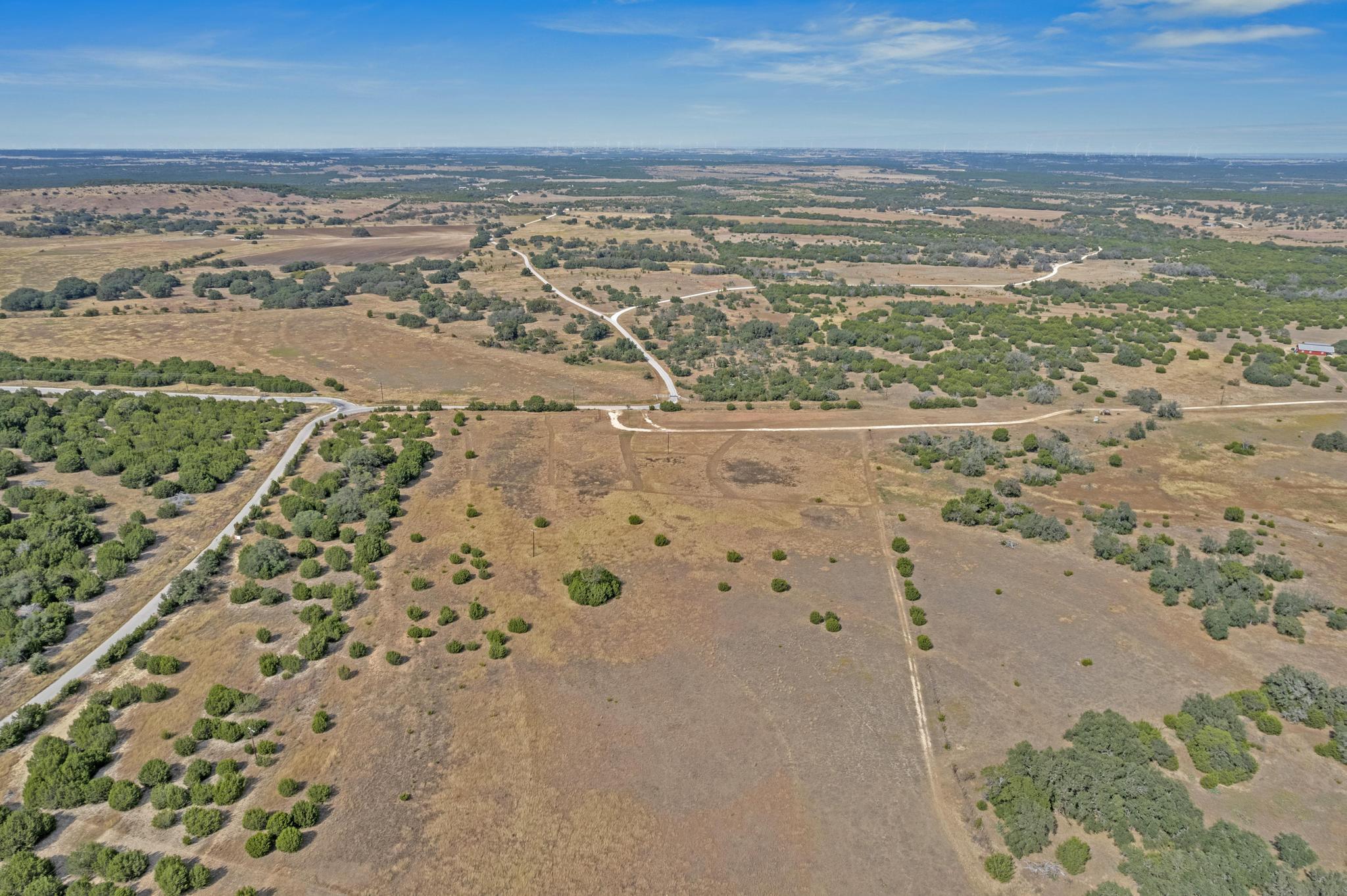 Aerial view of dry rural acreage with scattered brush, trees, and winding roads.