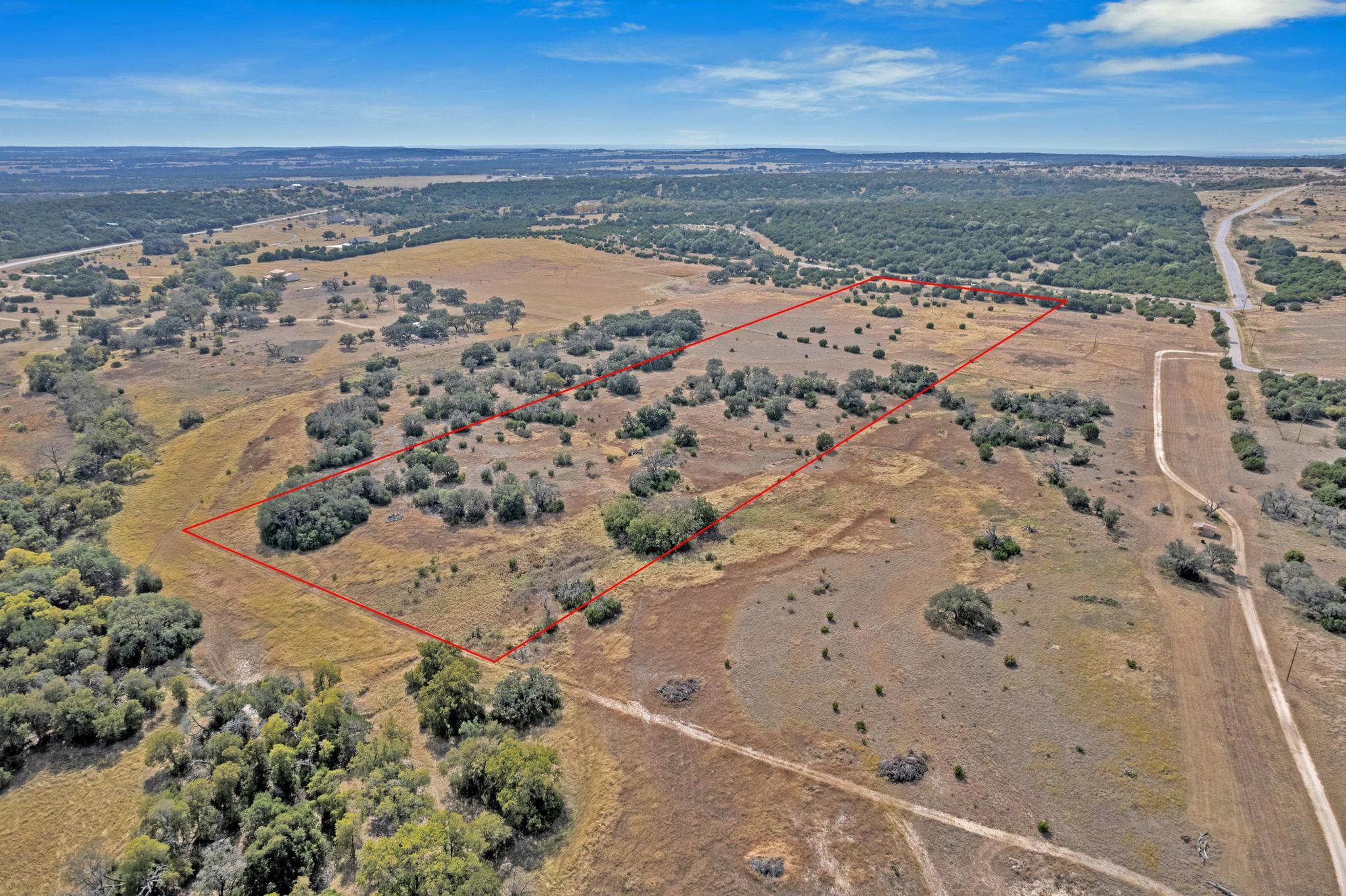 Aerial view of a rural, tree-dotted parcel outlined in red beside dirt roads.