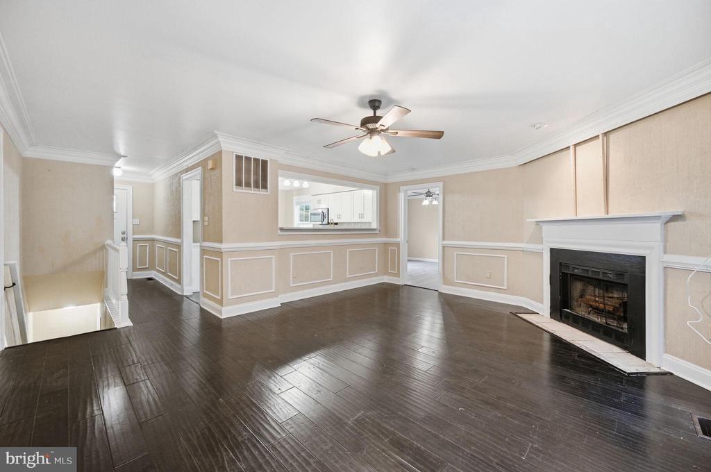 Empty living room with dark hardwood floors, a fireplace, and a pass-through to the kitchen.