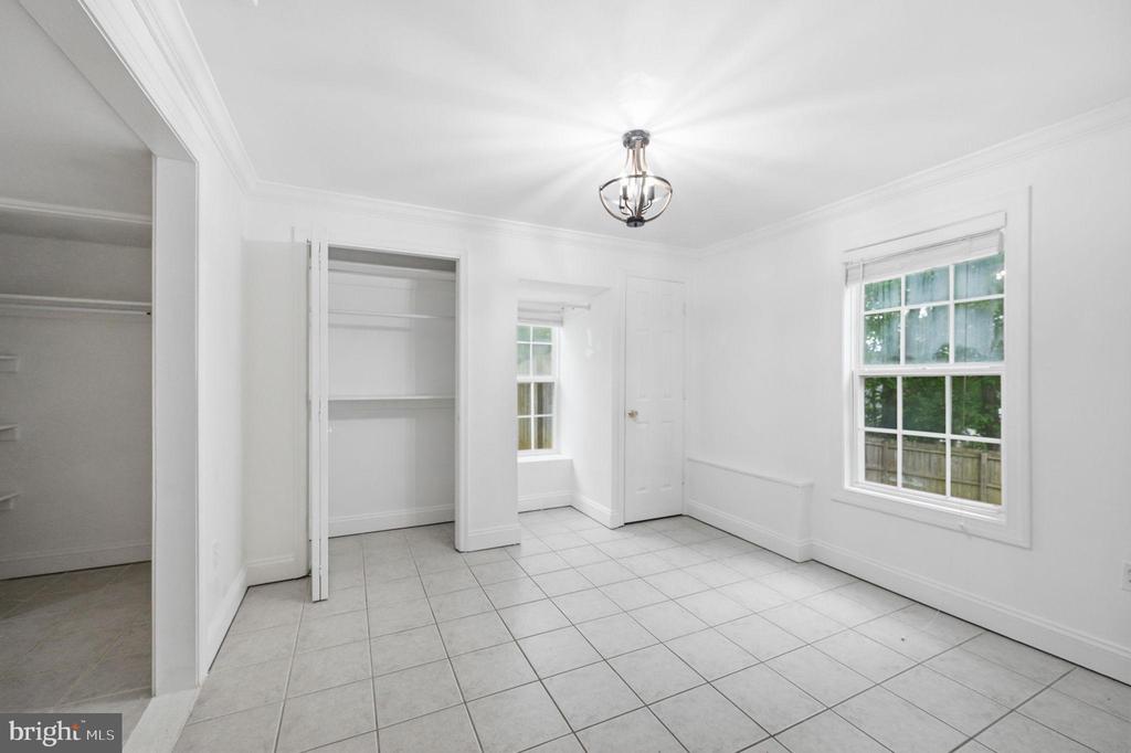 Vacant bedroom with an open closet, tiled floor, and two windows.