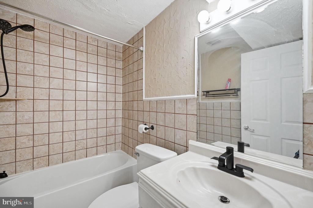 Bathroom with a tiled bathtub, white vanity sink, and large mirror.