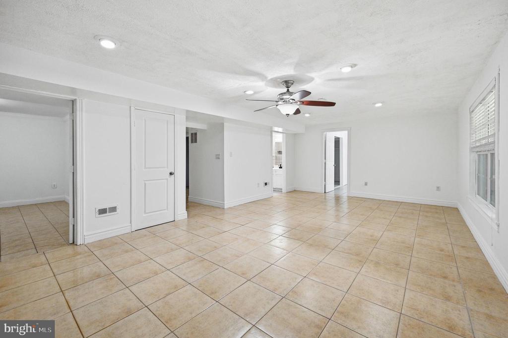 Empty tiled room with a ceiling fan, recessed lights, and several doorways.