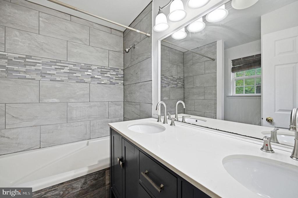 Bathroom with gray tiled walls, mosaic accent strip, and a dark double vanity with two sinks.