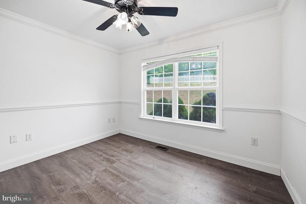 Empty bedroom with plank flooring, a ceiling fan, and a window overlooking a white picket fence.
