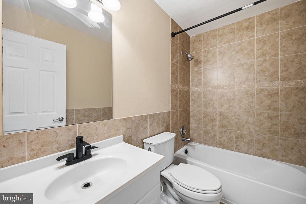 Bathroom with a white vanity, toilet, and bathtub surrounded by tan tile.