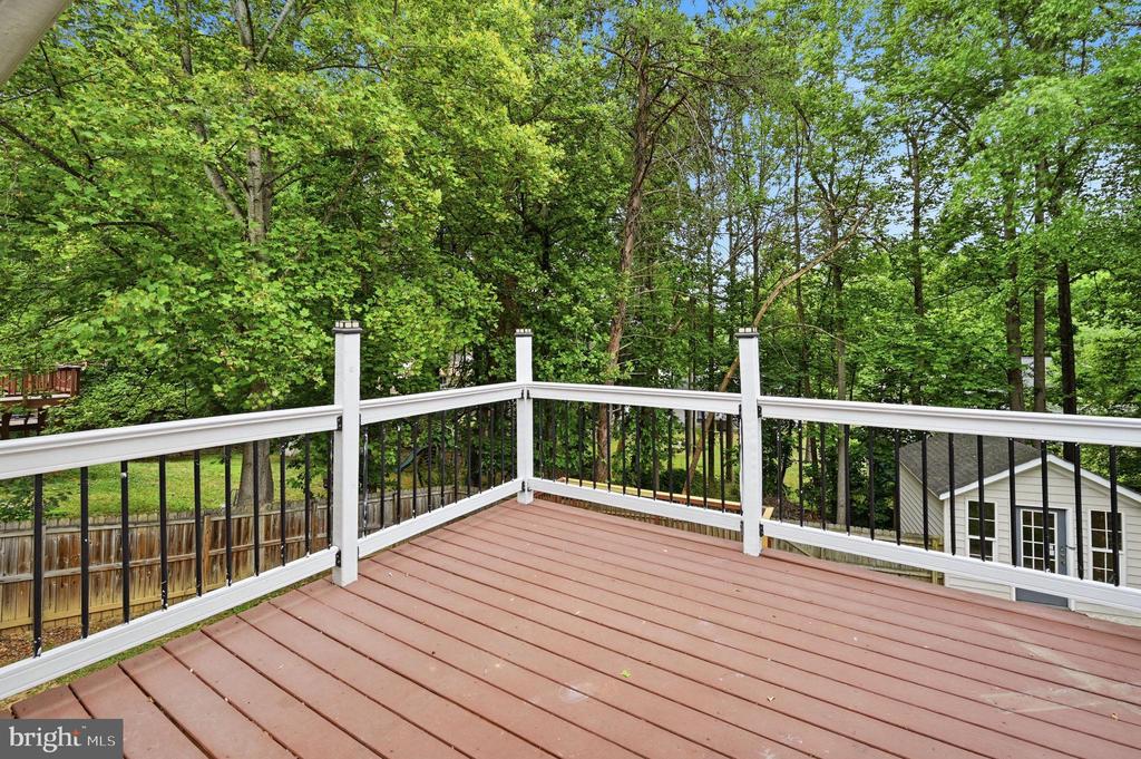 Deck with white railings overlooking a leafy wooded backyard.