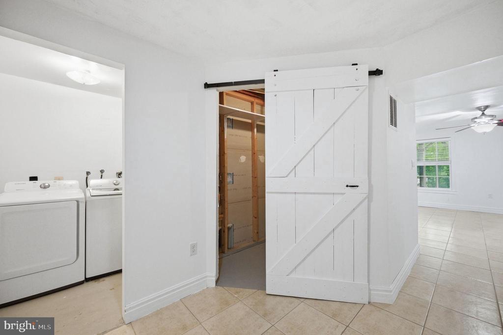 Laundry area with washer and dryer, beige tile floor, and a white sliding barn door.