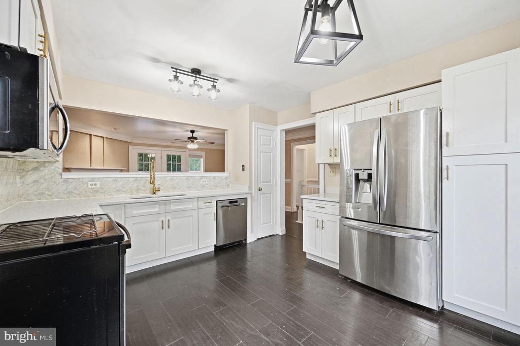Renovated kitchen with white cabinets, stainless steel appliances, stone counters, and dark tile flooring.