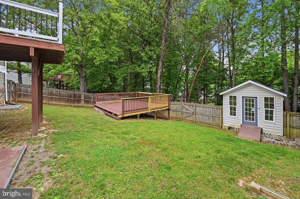 Fenced backyard with a raised deck, white shed, and mature trees.