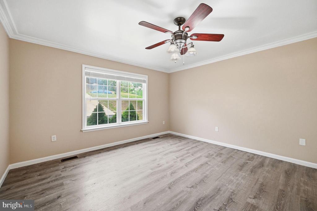 Empty bedroom with gray wood-look flooring, a large window, and a ceiling fan.