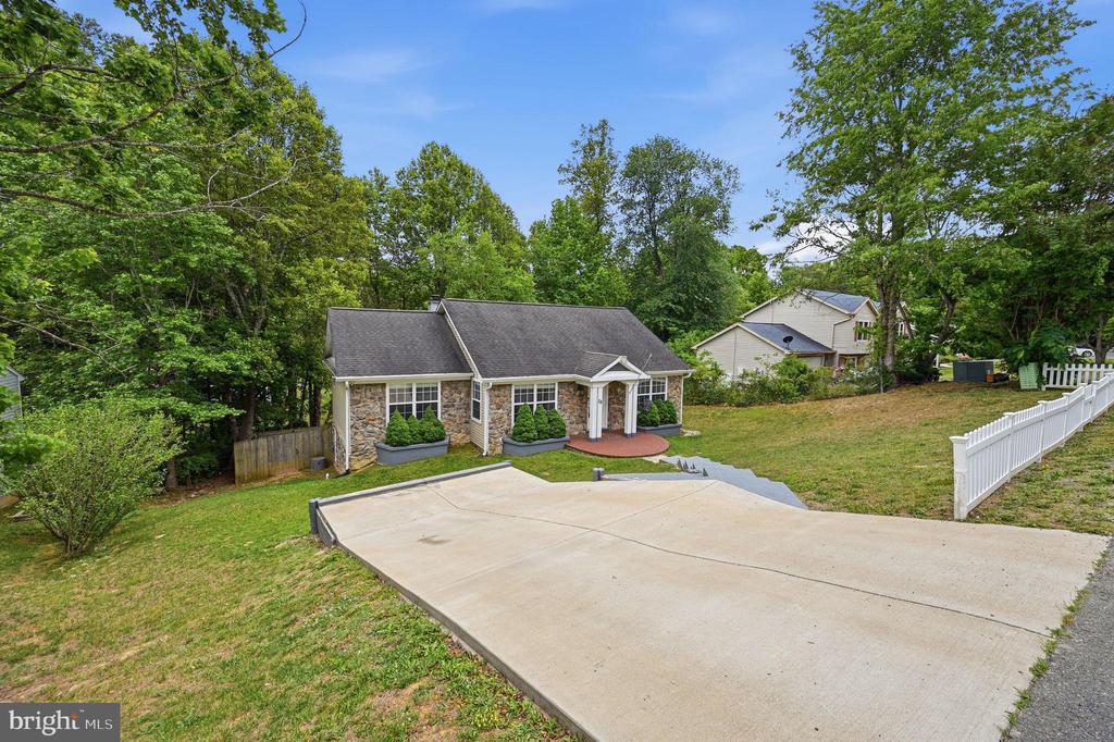 Stone-front home with a broad concrete driveway, grassy yard, and mature trees.