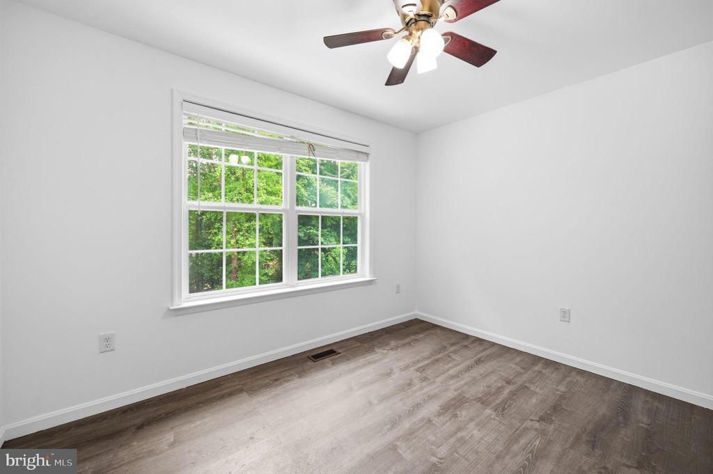 Vacant bedroom with a large window overlooking trees, gray wood-look flooring, and a ceiling fan.