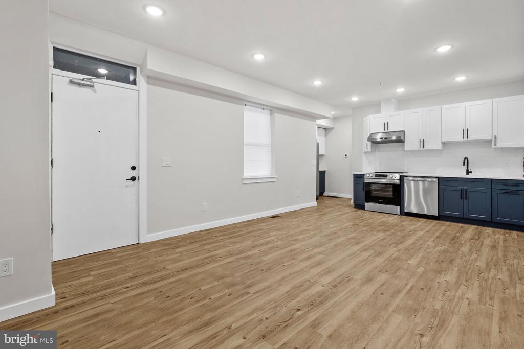 Empty open-plan kitchen with navy lower cabinets, stainless steel appliances, and light wood flooring.