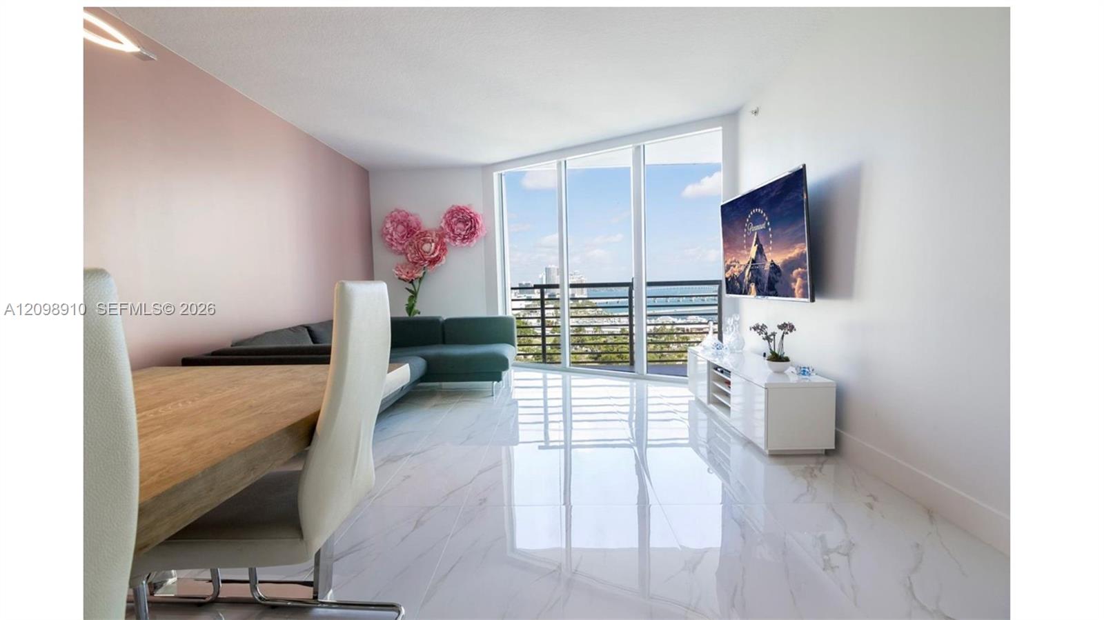 Furnished living and dining area with floor-to-ceiling windows overlooking water and the city.