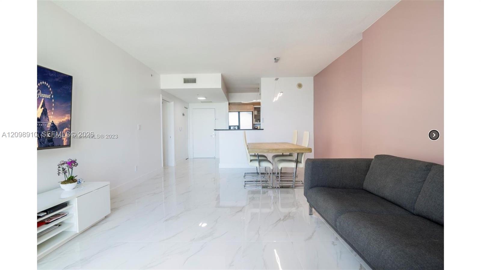 Condo living and dining area with glossy marble-look floors, a gray sofa, and a pink accent wall.