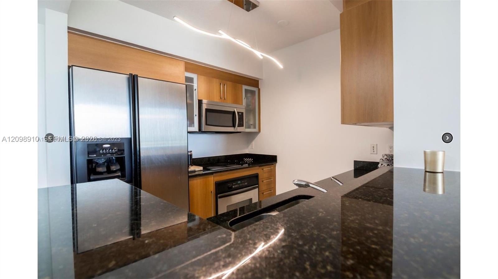 Modern condo kitchen with granite counters, warm wood cabinets, and stainless steel appliances.