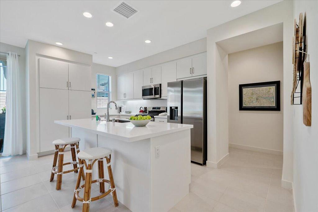 Bright white kitchen with a large island, stainless steel appliances, and two counter stools.
