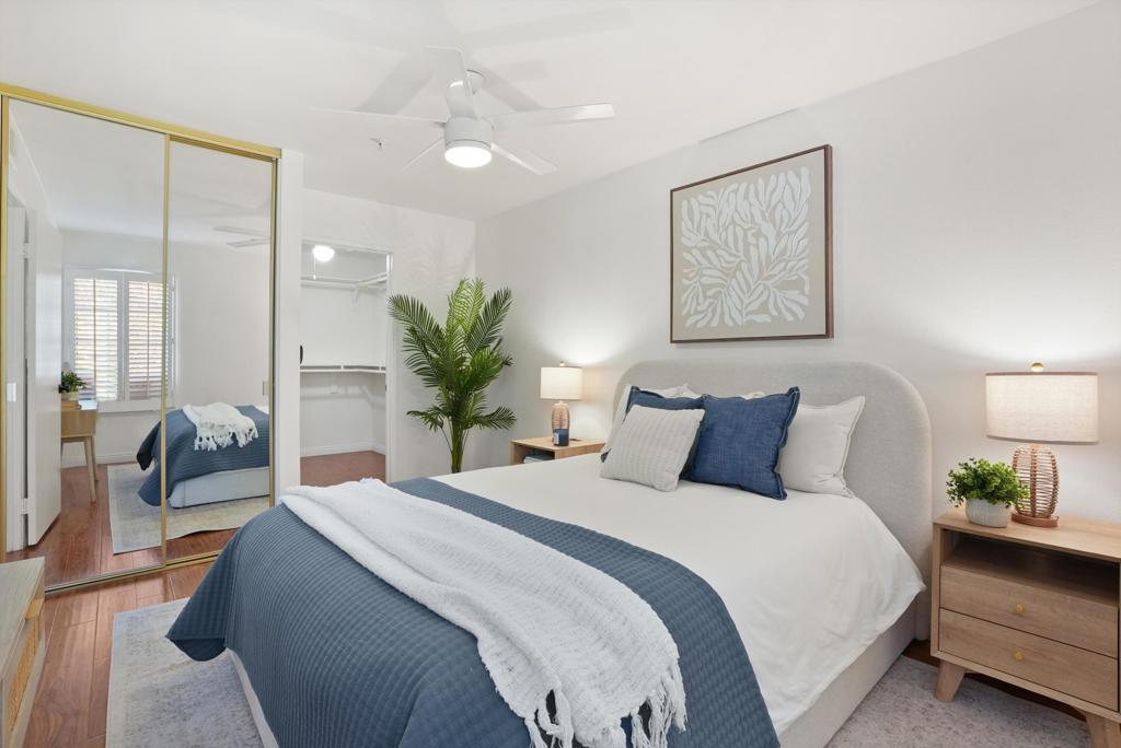 Staged bedroom with blue bedding, mirrored closet doors, and a ceiling fan.