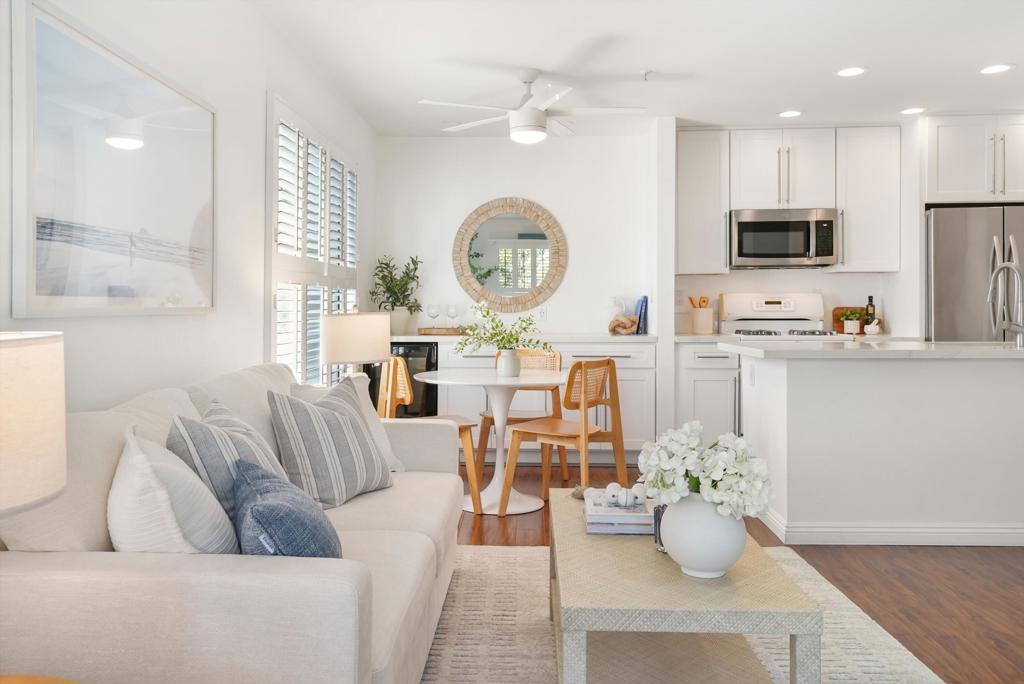 Open-plan living room and kitchen with a white sofa, round dining table, and stainless steel appliances.