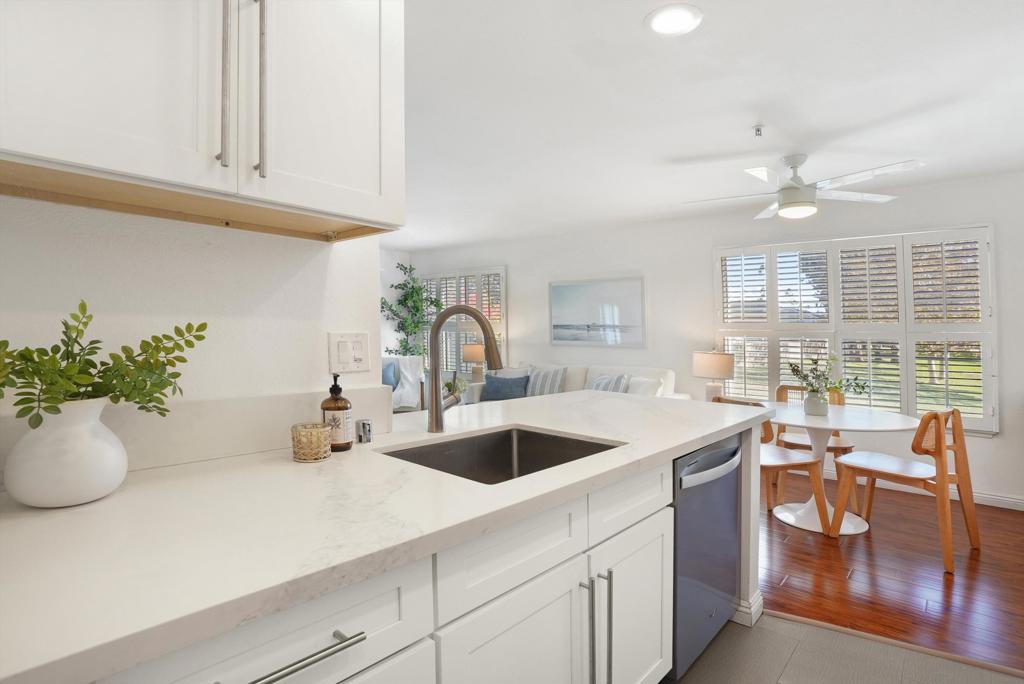 Bright kitchen with a white quartz island, stainless-steel dishwasher, and dining area by shuttered windows.