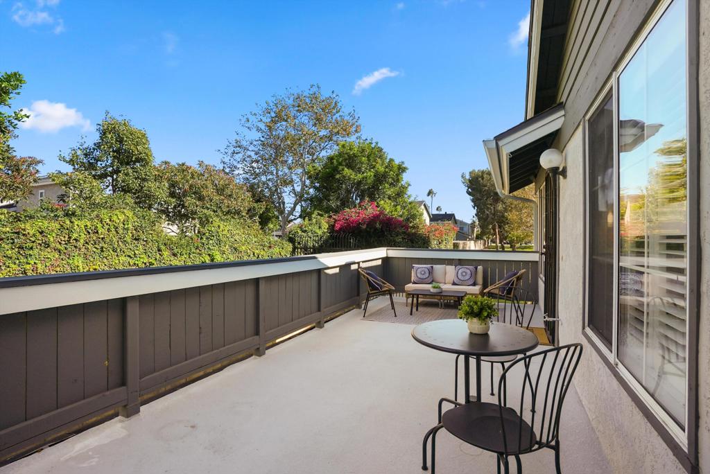 Furnished balcony patio with a round table, chairs, and leafy privacy hedge.